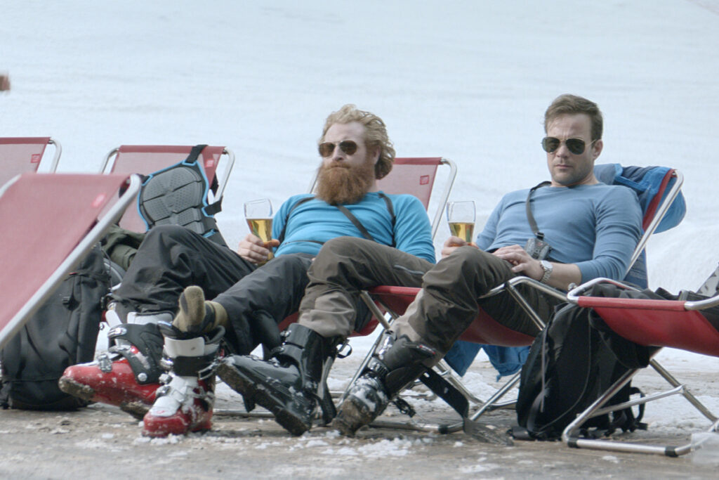 Force Majeure | Ruben Ostlund Force Majeure movie still. Two men in ski boots sit in chairs, drinking beer on a snowy mountain.