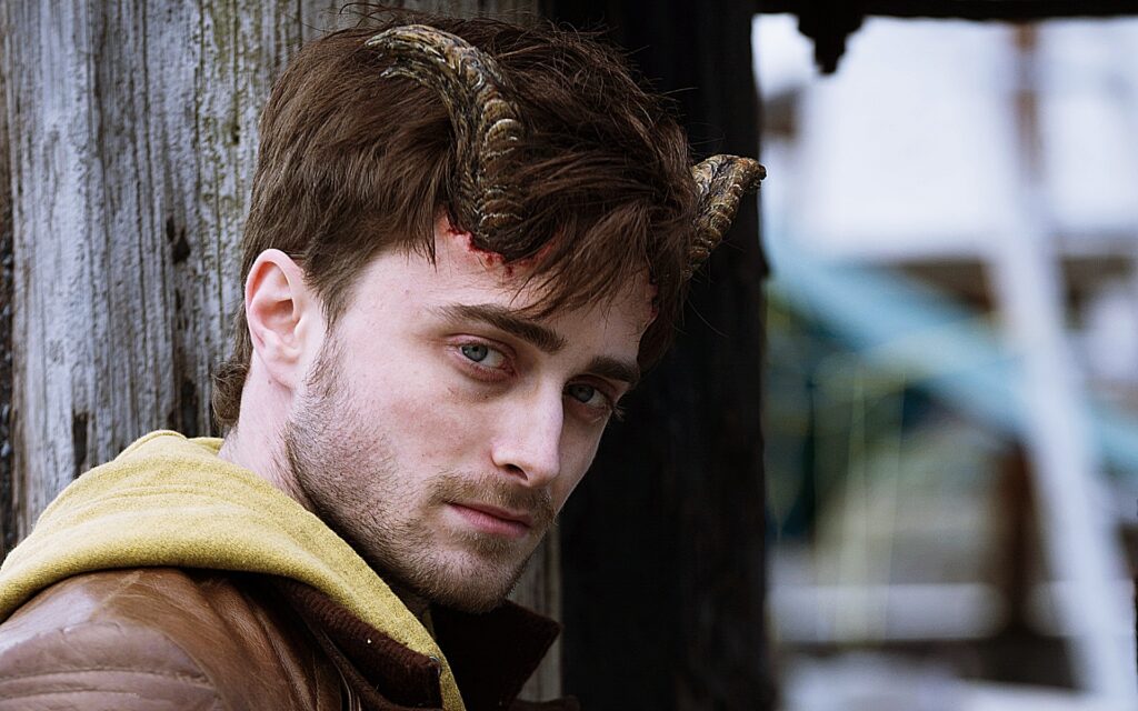 Daniel Radcliffe in Horns. Actor with devil horns, brown hair, and leather jacket. Alexandre Aja film.
