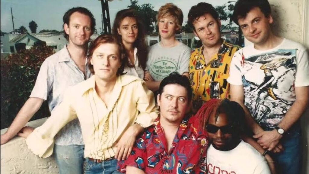 The Mekons band photo. The Mekons Rock N’ Roll band members pose together in colorful shirts.