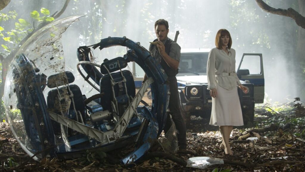 Jurassic World scene with Chris Pratt, Bryce Dallas Howard, gyrosphere wreckage, and SUV in a jungle setting.