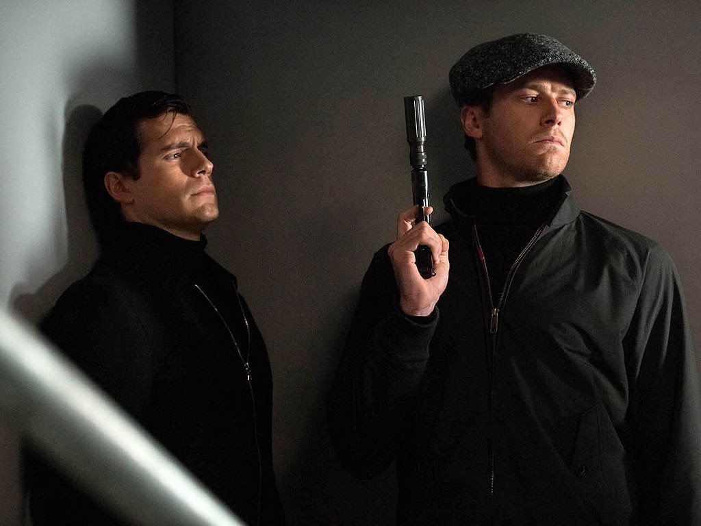 The Man from U.N.C.L.E. film still. Henry Cavill and Armie Hammer as spies, one holding a gun. Guy Ritchie film.