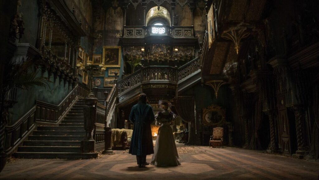 Crimson Peak | Guillermo del Toro Crimson Peak movie scene. Couple stands in grand, gothic hall with ornate staircase and dark, decaying decor. Guillermo del Toro film.