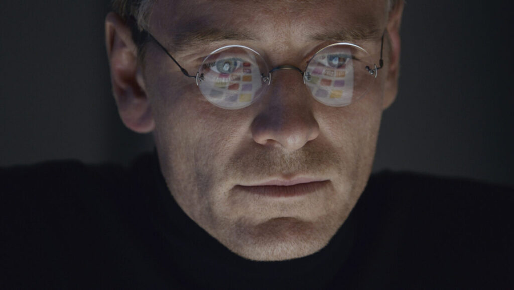 Michael Fassbender as Steve Jobs. The reflection in his glasses shows a computer screen.