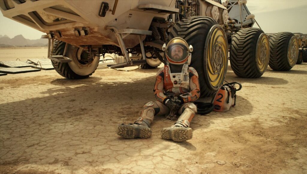 Matt Damon as Mark Watney in Ridley Scott's The Martian movie. Astronaut sitting on Mars with rover.