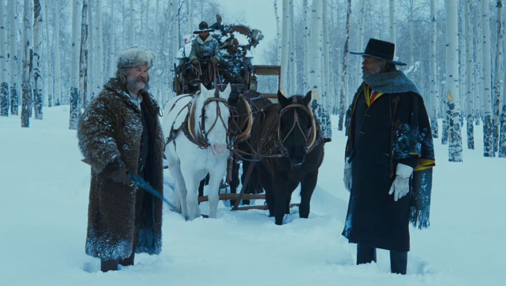 The Hateful Eight: Kurt Russell and Samuel L. Jackson stand in a snowy forest next to a horse-drawn carriage.