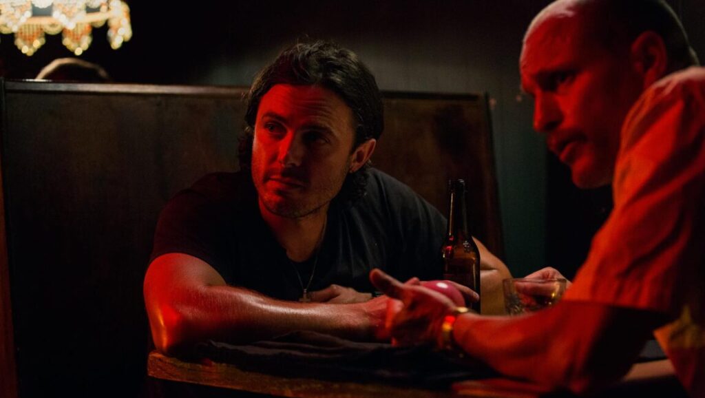 Casey Affleck in Triple 9 (2016) movie scene. Two men in a dimly lit booth with a beer bottle. John Hillcoat film.