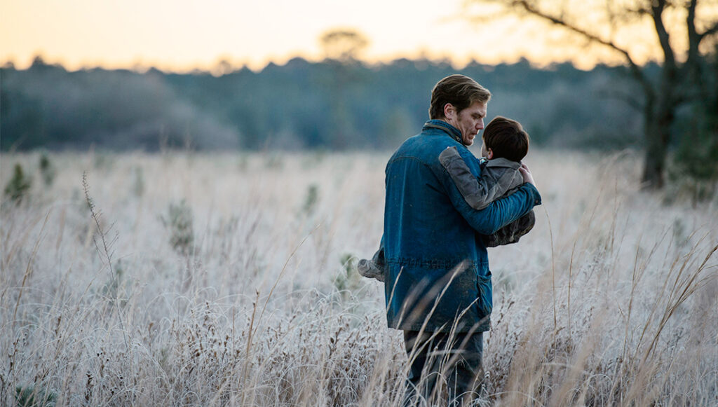Midnight Special movie scene. Father carrying his son in a field at dusk.