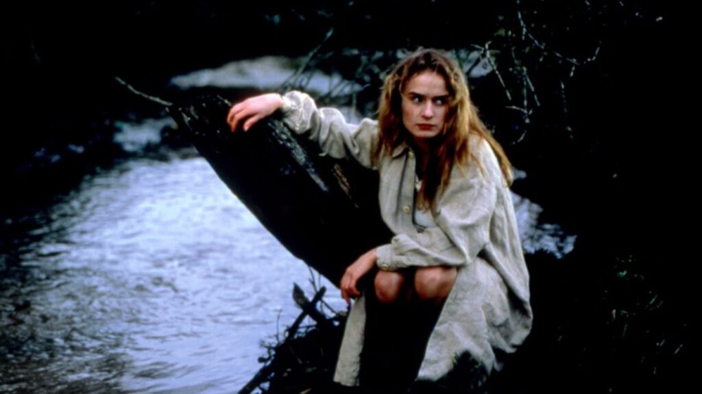 Under the Sun of Satan film still. Woman in coat sits by a river, part of BAMcinématek's Booed at Cannes series.