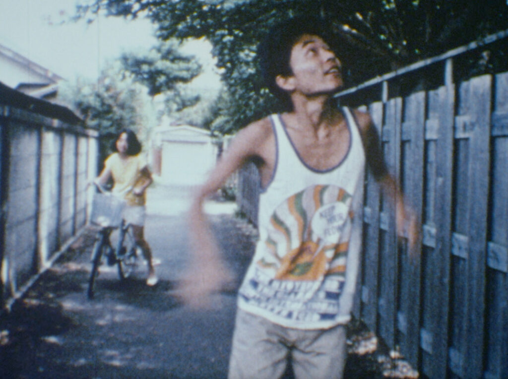 Sion Sono's A Man's Flower Road film still. Man in tank top, woman on bike in alley.