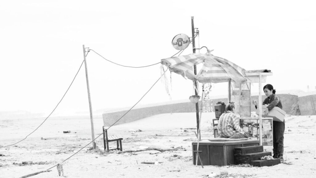 Black and white still from Whispering Star, Japan Cuts 2016 film festival. Woman and man at a small roadside stall.
