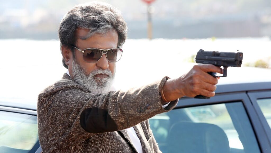 Rajinikanth in Kabali. Actor with gun, wearing sunglasses and tweed jacket.