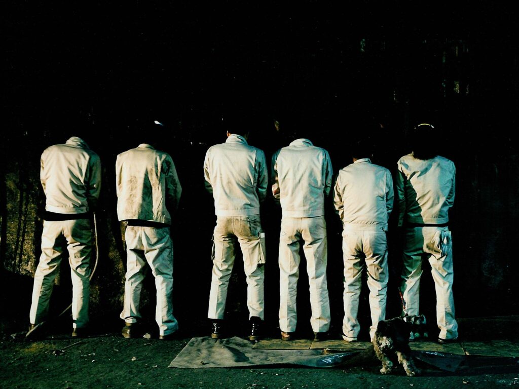 Into a Dream film still: Six men in white uniforms urinating against a dark wall.