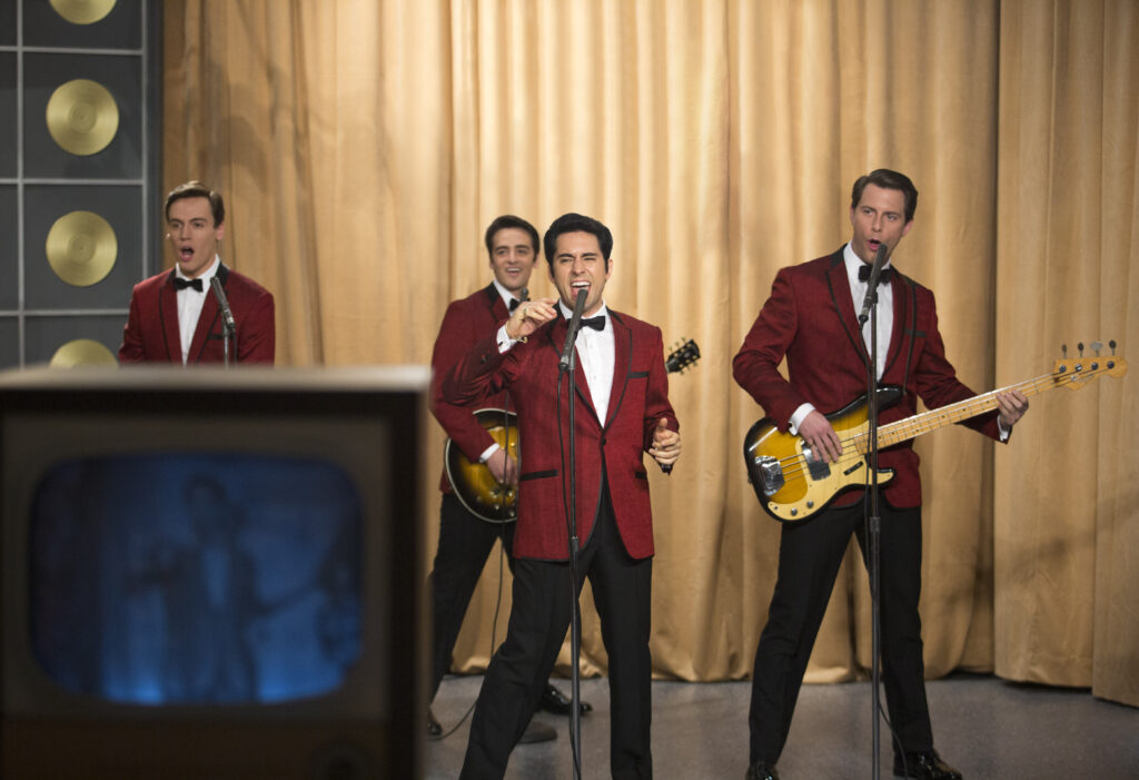 Jersey Boys cast performing. The Four Seasons tribute band in red suits sing and play instruments. Clint Eastwood film.