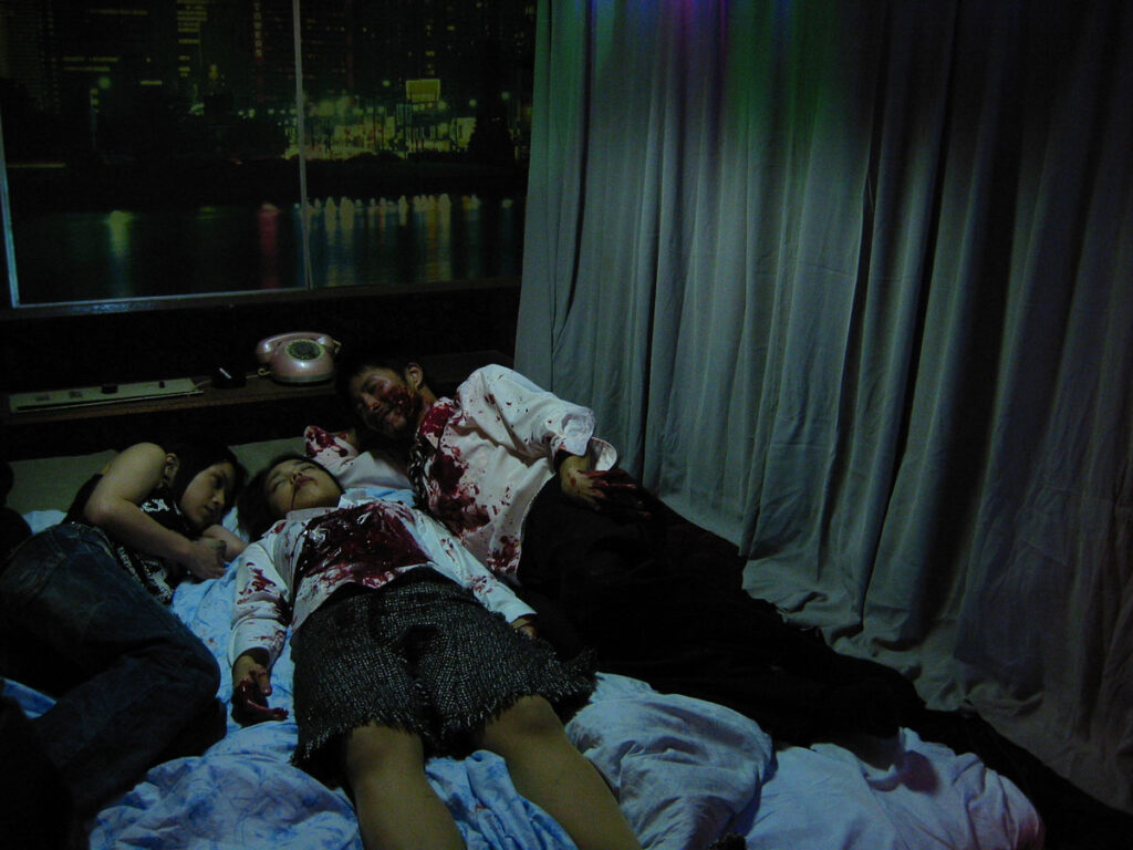 Noriko’s Dinner Table | Sion Sono Noriko's Dinner Table film still. Three people covered in blood lie on a bed.