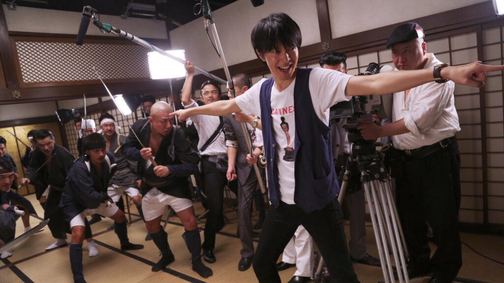 Behind the scenes of Why Don't You Play in Hell? Sion Sono directs sword-wielding actors on a film set.
