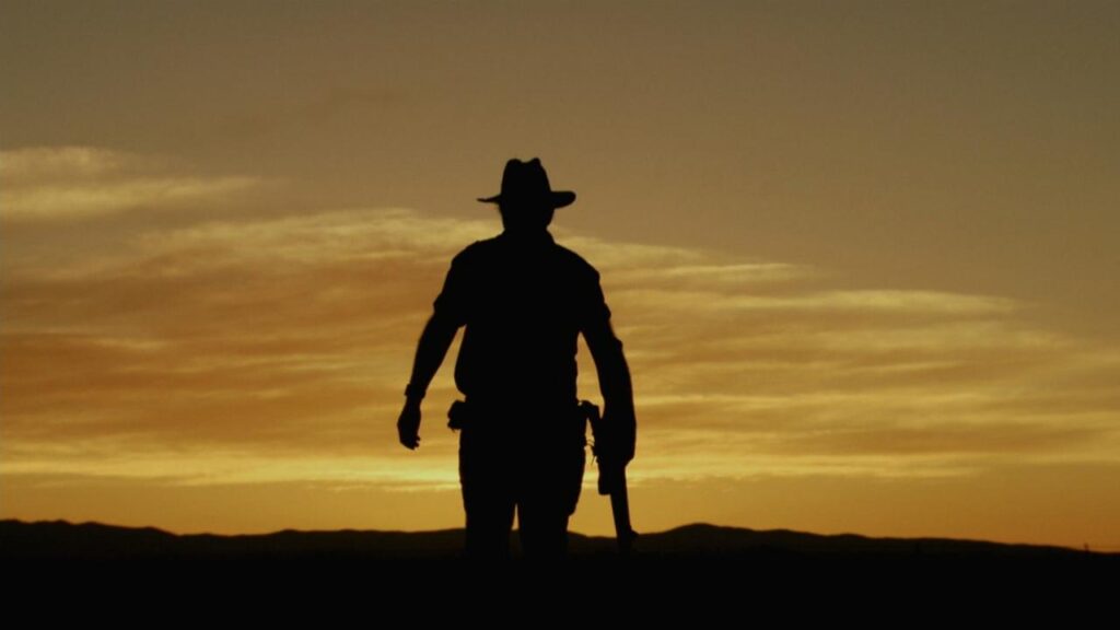 Wolf Creek horror movie banner. Silhouette of Mick Taylor at sunset. Best horror of the 2000s.