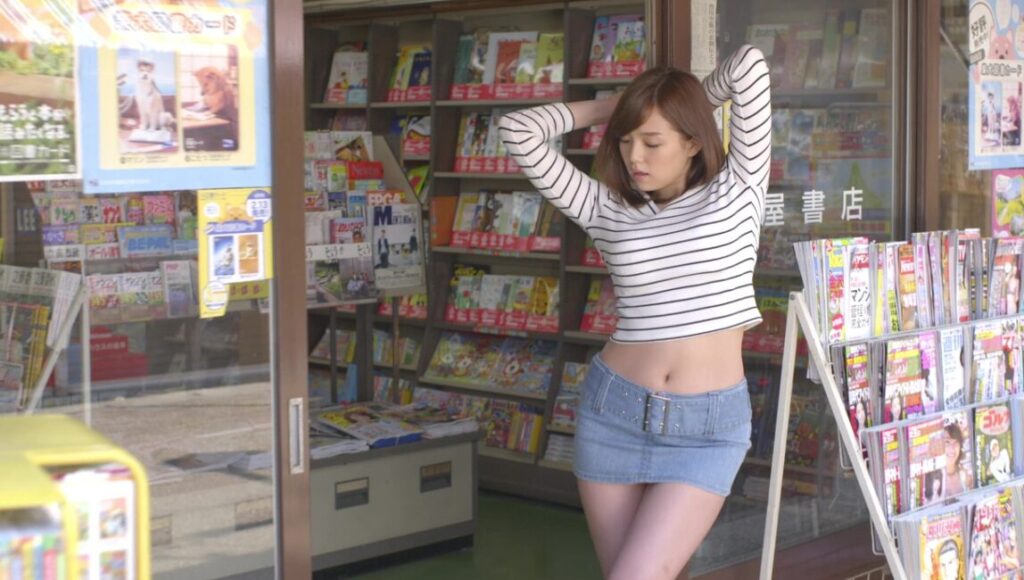 The Virgin Psychics | Sion Sono Virgin Psychics film still: Woman in striped top and denim skirt poses in front of a bookstore.