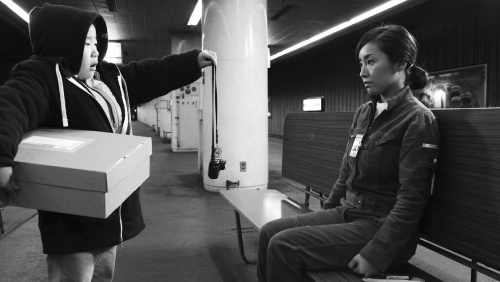 The Whispering Star | Sion Sono The Whispering Star film still. Black and white image of a delivery to a woman. Sion Sono film.
