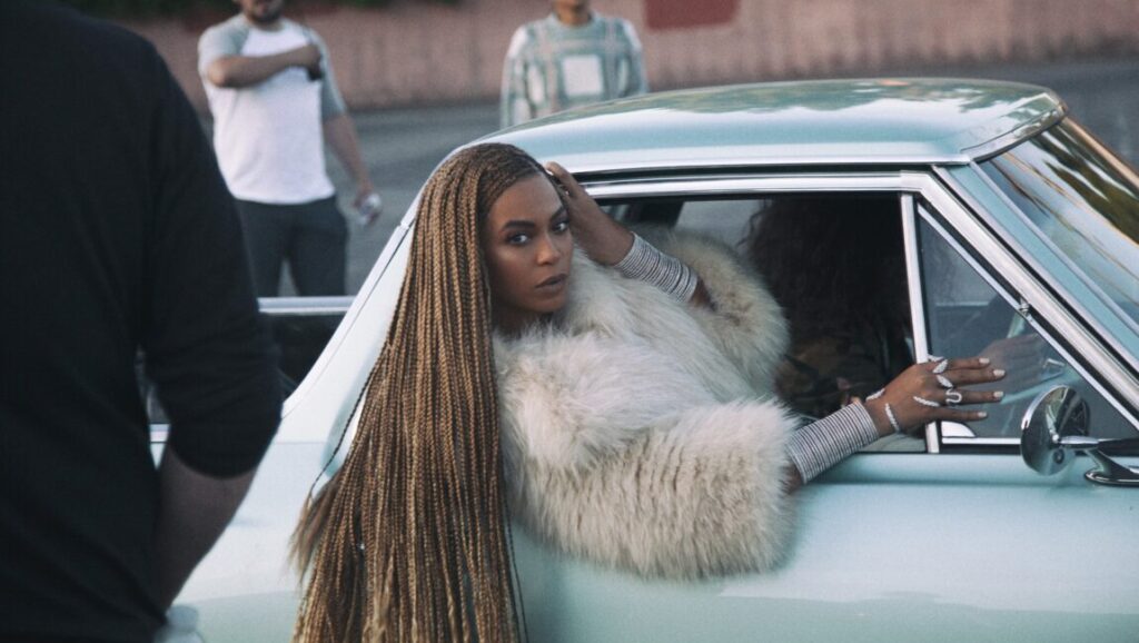 Top 10 Songs of 2016 Beyoncé in Formation music video, a top song of 2016. Singer in fur coat leaning out of car.