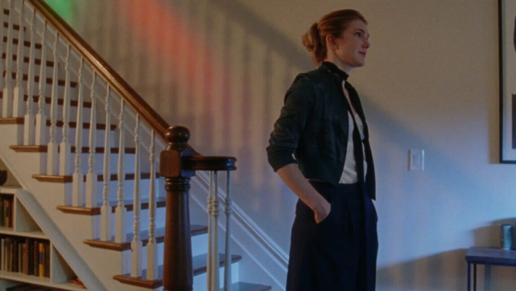 Golden Exits film still at BAMcinemaFest 2017. Woman stands near a staircase, lit by colorful light.