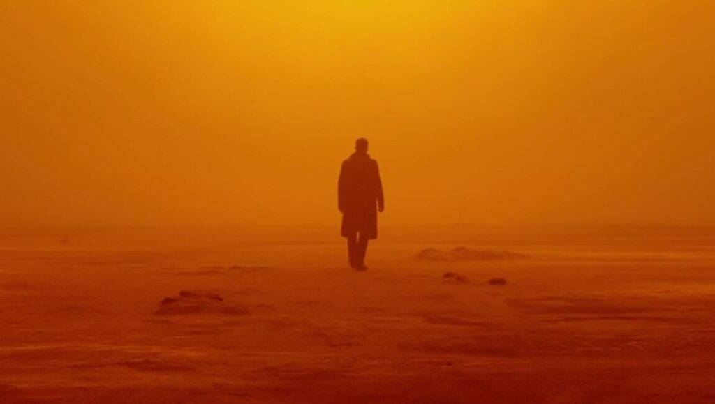 Blade Runner 2049 | Denis Villeneuve Blade Runner 2049: Silhouette of Ryan Gosling's character, Officer K, walking through an orange, dusty landscape.