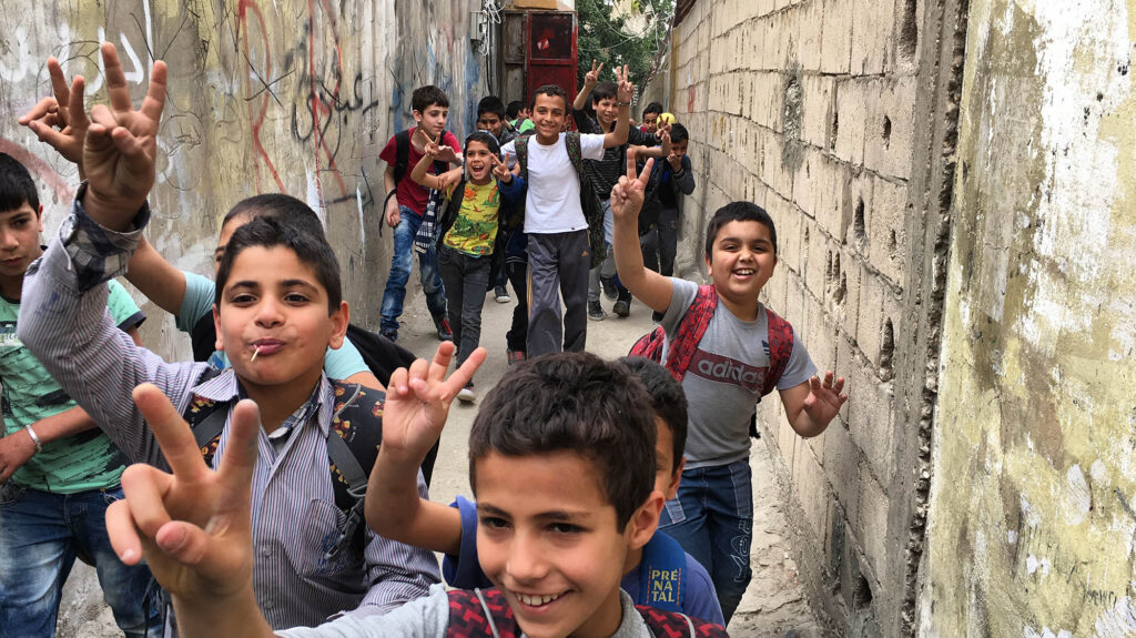 Refugee children in Ai Weiwei's Human Flow documentary flash peace signs in a narrow alleyway. Hopeful faces.