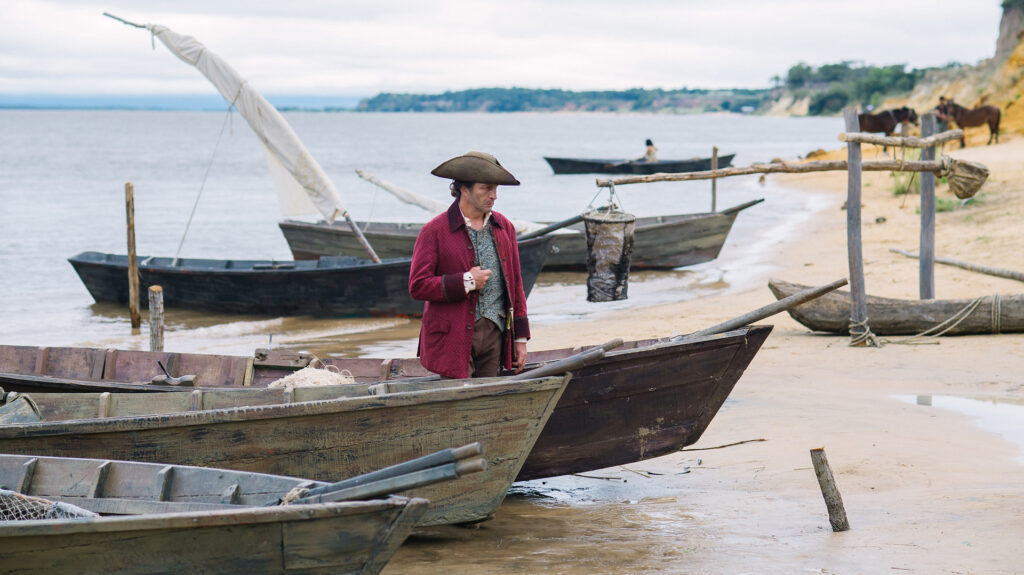 New York Film Festival 2017 – Dispatch 3 Scene from Zama at New York Film Festival 2017. Man in period clothing stands near boats on a sandy beach.
