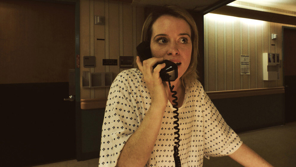 Claire Foy in Unsane on a phone. Foy wears a hospital gown, looking distressed in the Steven Soderbergh thriller.