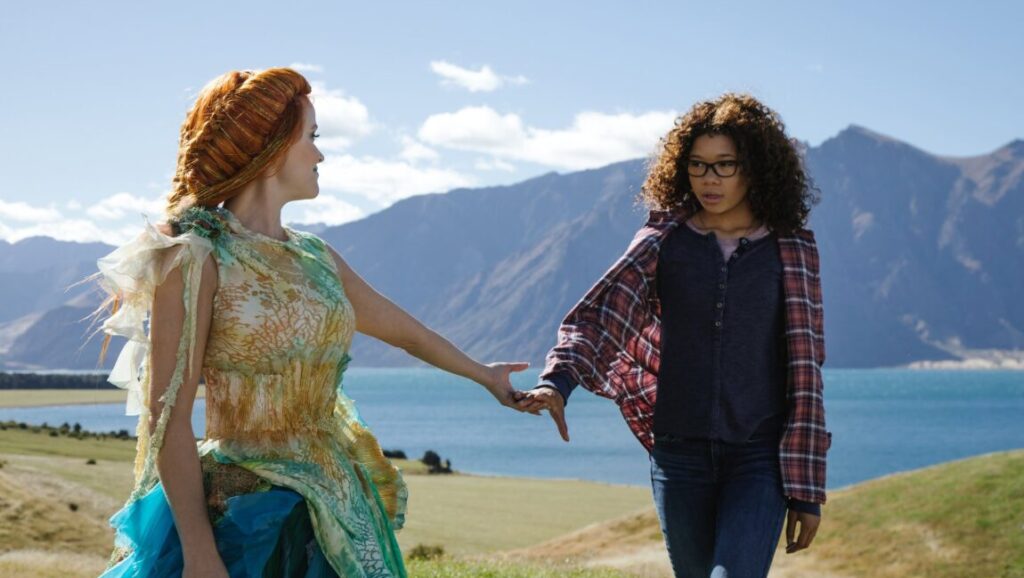 A Wrinkle in Time | Ava DuVernay A Wrinkle in Time movie scene: Reese Witherspoon and Storm Reid on a hill with mountains and a lake in the background.