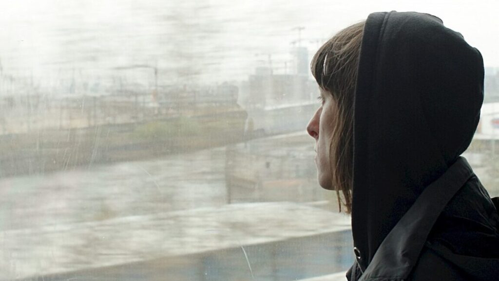 Woman in hoodie looks out rainy window on train. Travel, reflection.