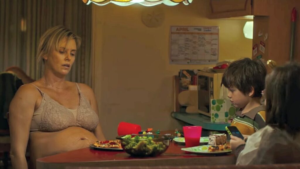 Charlize Theron as Tully, pregnant and exhausted, sits at a table with her children in the Jason Reitman film.