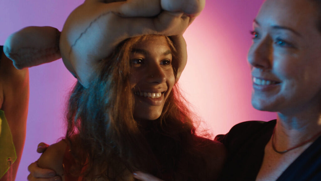 BAMcinemaFest 2018: Smiling woman with puppet headpiece at film festival event, illuminated by pink and blue lighting.