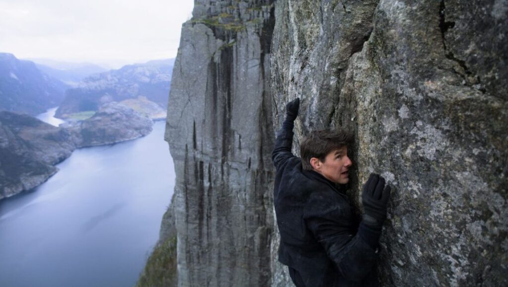 Tom Cruise climbing a cliff in Mission: Impossible - Fallout. Action movie scene.
