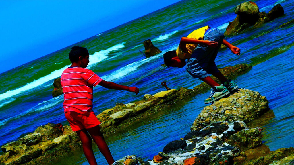 Scene from Toronto Film Festival: Two boys on rocks by the sea. One boy reaches out to help the other.