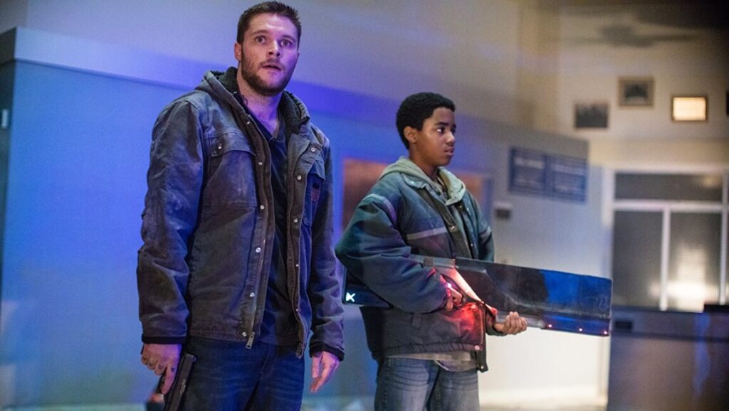 Kin movie scene. Jack Reynor and Myles Truitt star in the sci-fi action film. Truitt holds a futuristic weapon.