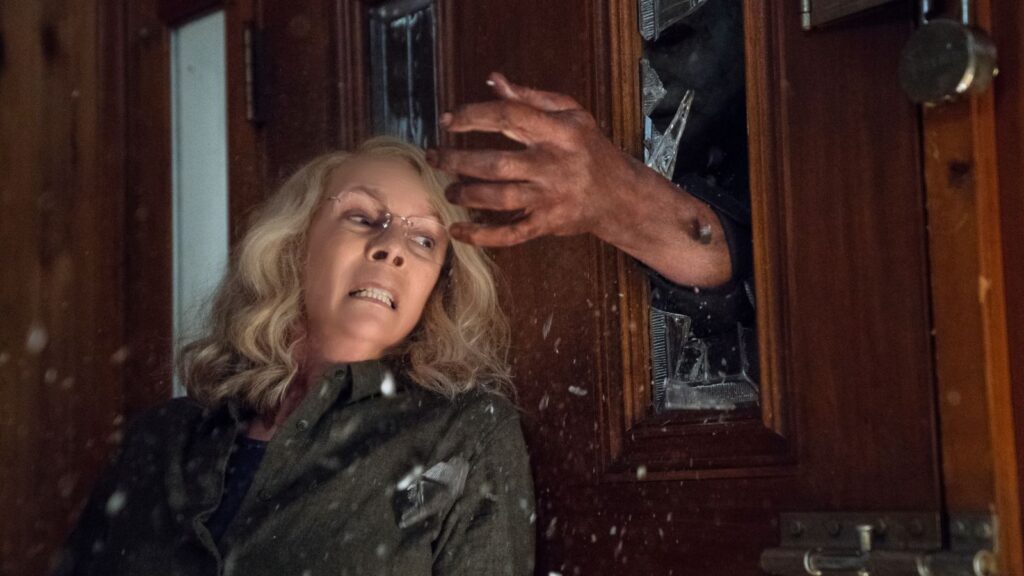 Jamie Lee Curtis in Halloween (2018) at TIFF. Michael Myers' hand reaches through a broken door. Horror film.