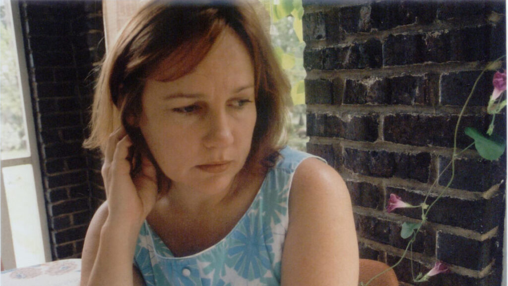 Iris DeMent portrait. Singer-songwriter in floral dress with hand to ear. My Life album.