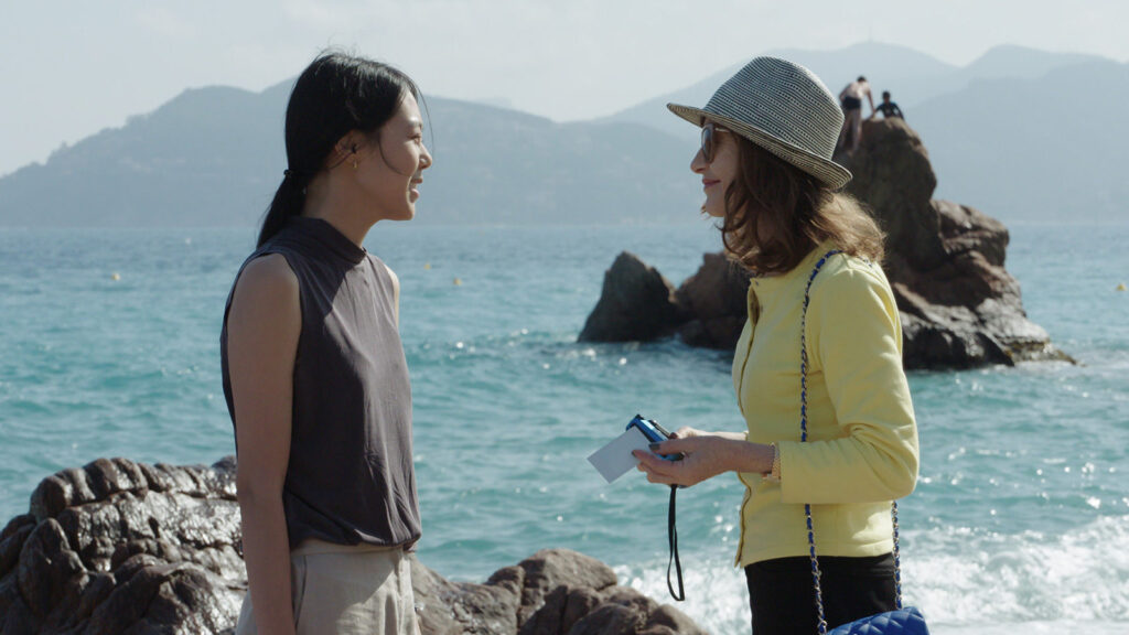 Claire’s Camera | Hong Sang-soo Isabelle Huppert in Claire's Camera by Hong Sang-soo. Two women chat, ocean backdrop. Cannes Film.