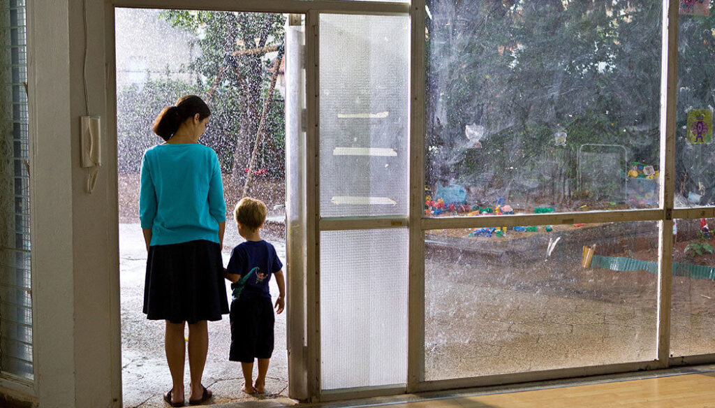 The Kindergarten Teacher film scene: Teacher and child looking at rain through a window. Nadav Lapid movie.
