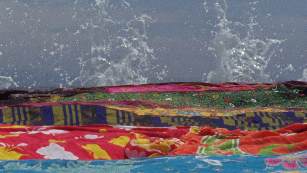 Still from New York Film Festival: A colorful textile foreground with ocean waves crashing in the background.