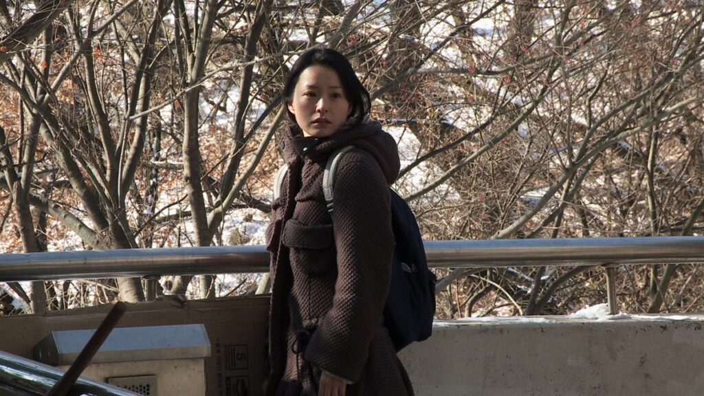 Oki’s Movie | Hong Sang-soo Park Hyo-joo in Oki's Movie. Still from Hong Sang-soo's film. Woman in winter coat with trees in background.