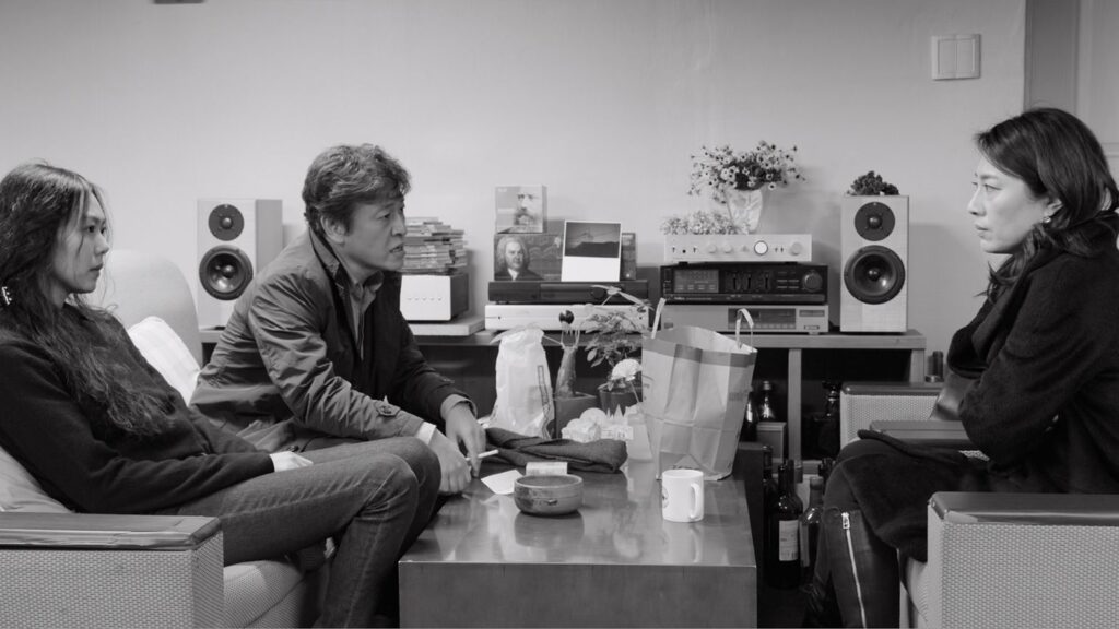 The Day After | Hong Sang-soo The Day After film still. Black and white image of three people in a living room. Hong Sang-soo movie.