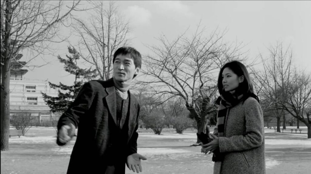 Black and white still from Virgin Stripped Bare by Her Bachelors, featuring two actors in a park.