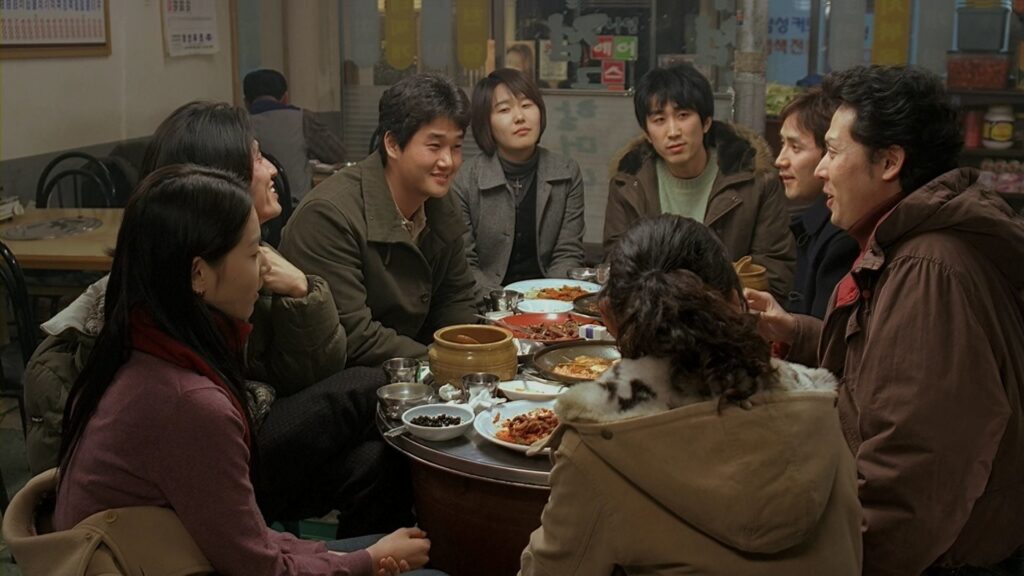 Woman Is the Future of Man film scene. Group of Korean people eating around a table. Hong Sang-soo movie.