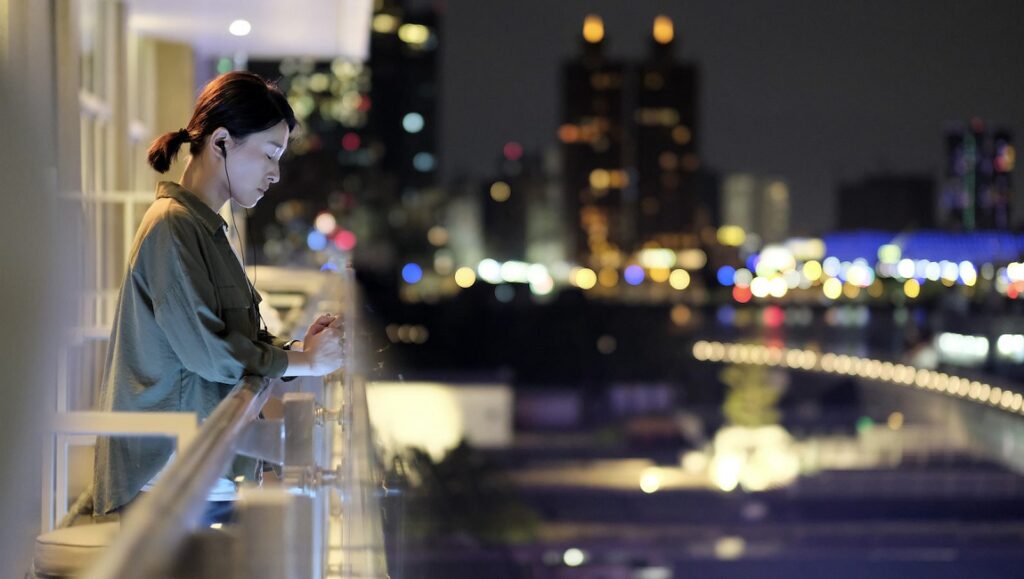 A Family Tour | Ying Liang Woman on balcony at night in A Family Tour movie. City skyline in background. Ying Liang film.