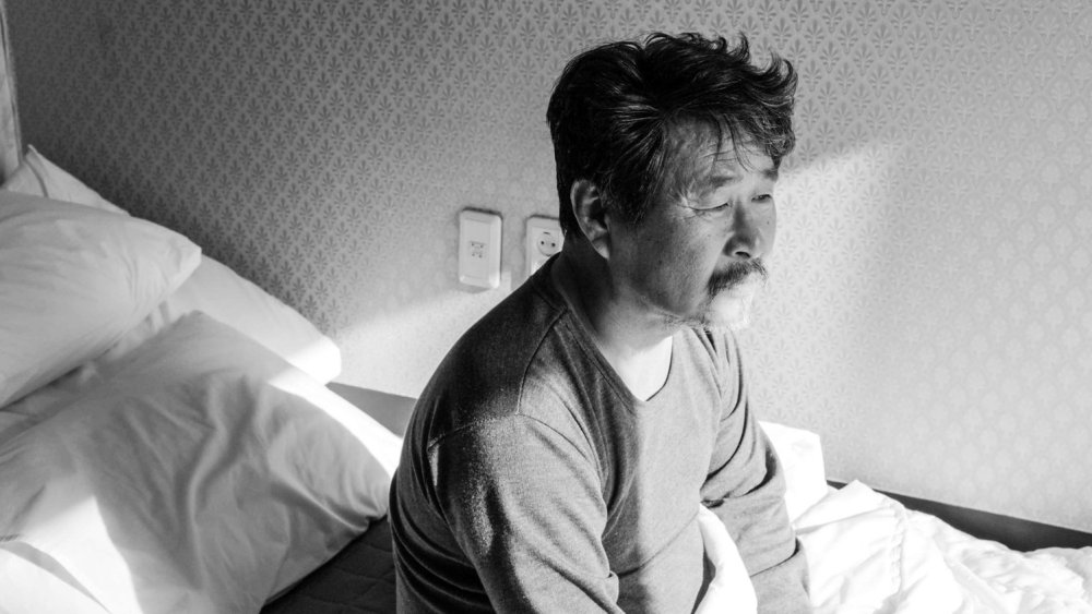 Hotel by the River | Hong Sang-soo Hotel by the River film still. An old man sits on a bed in a hotel room. Black and white.