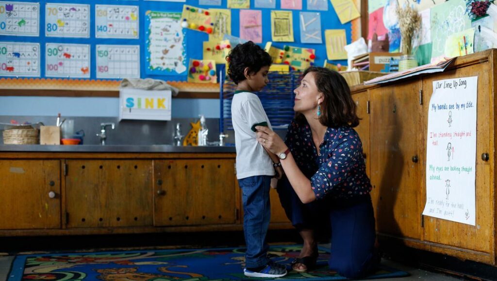 The Kindergarten Teacher movie scene. Teacher kneels, comforting a young student in a classroom.