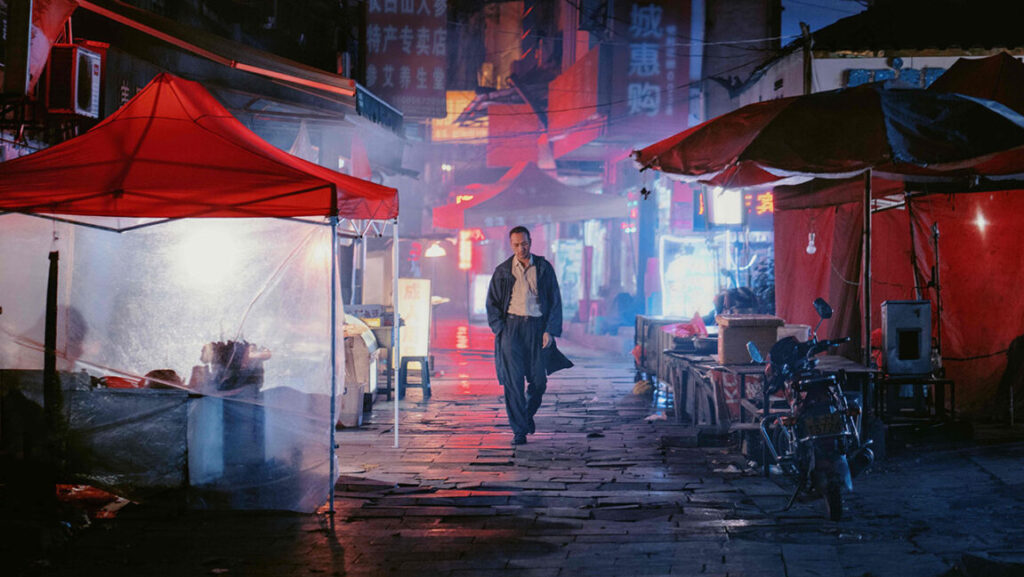 Scene from Long Day's Journey Into Night at New York Film Festival 2018. Man walks down neon-lit street.