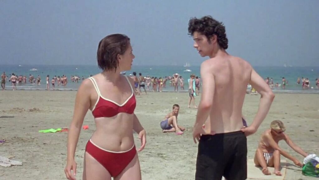 A Summer's Tale film still. Woman in red bikini and man on crowded beach. Eric Rohmer movie.