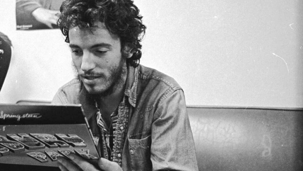 Bruce Springsteen holding the Nebraska album cover in a black and white photo.